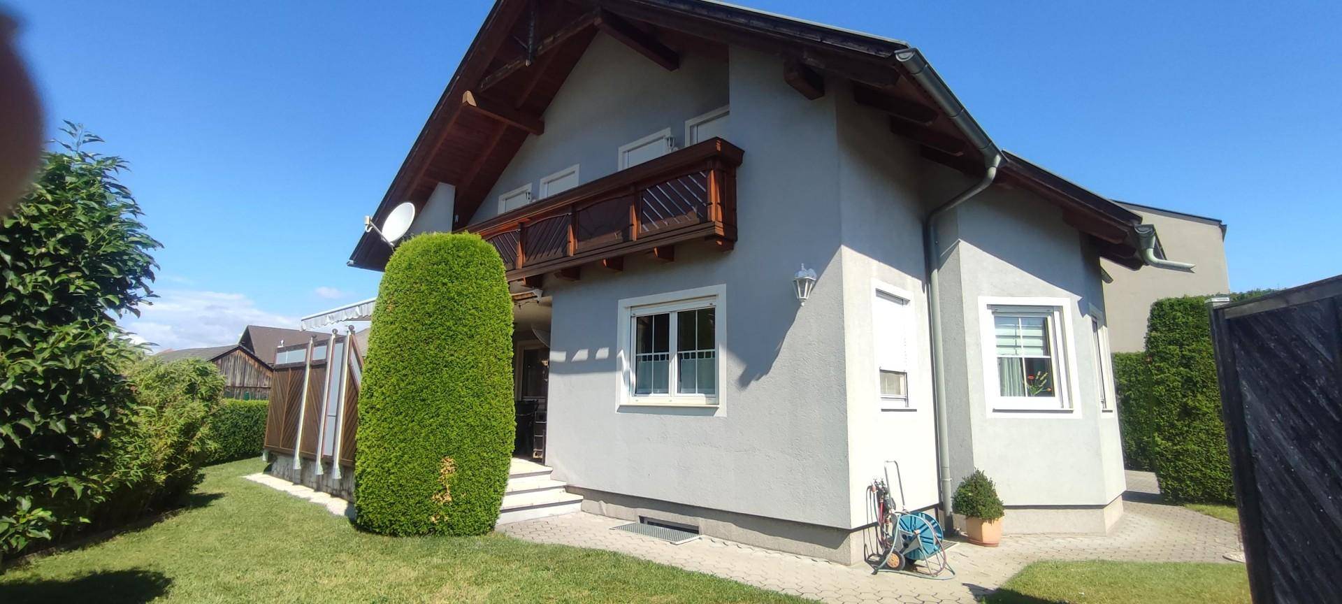 Seitenansicht des Hauses mit grünem Rasen, Hecke und einem kleinen Balkon im Obergeschoss.