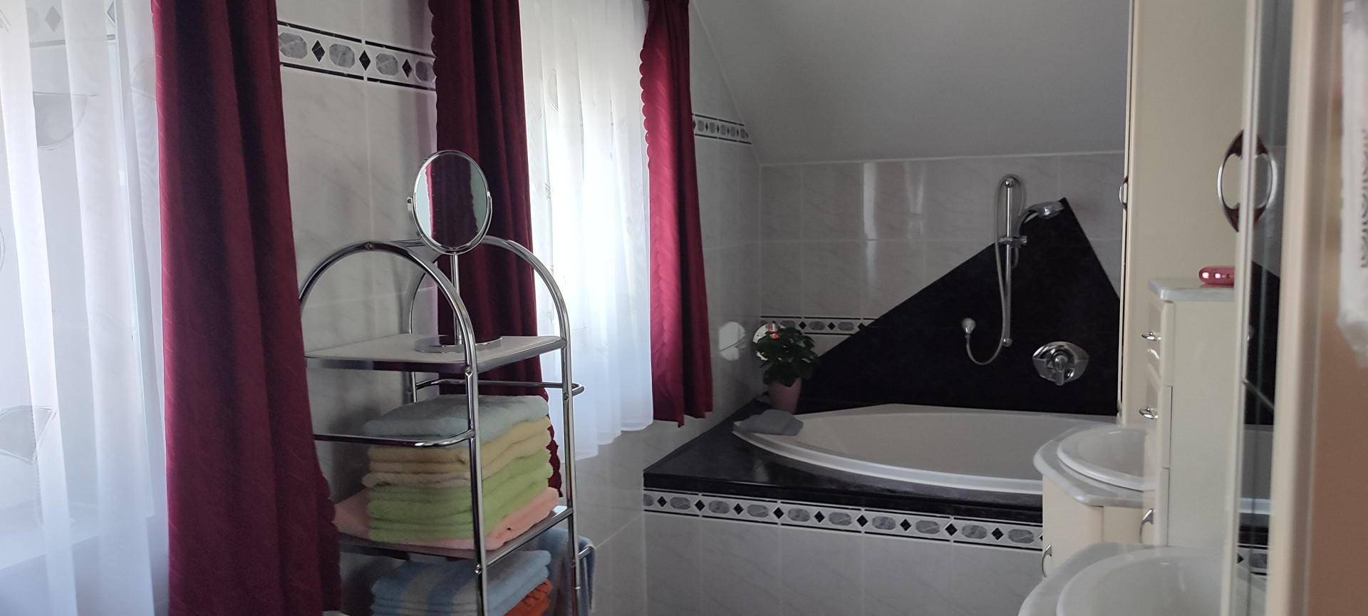 Badezimmer mit Eckbadewanne, Fliesenboden und Fenster mit roten Vorhängen.