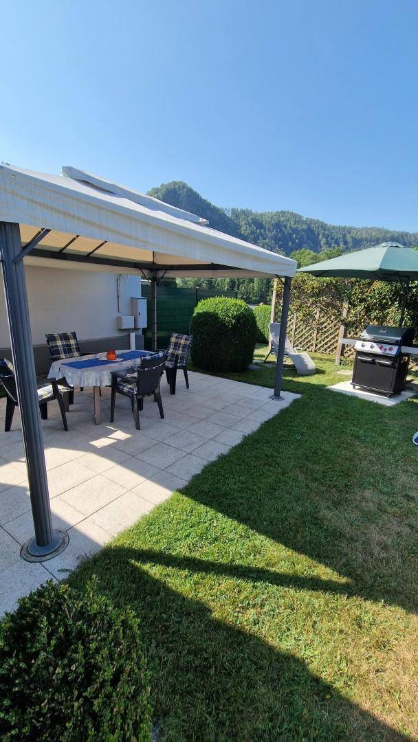 Gepflegter Garten mit überdachter Terrasse, Grillplatz und weitem Blick auf die Berge.