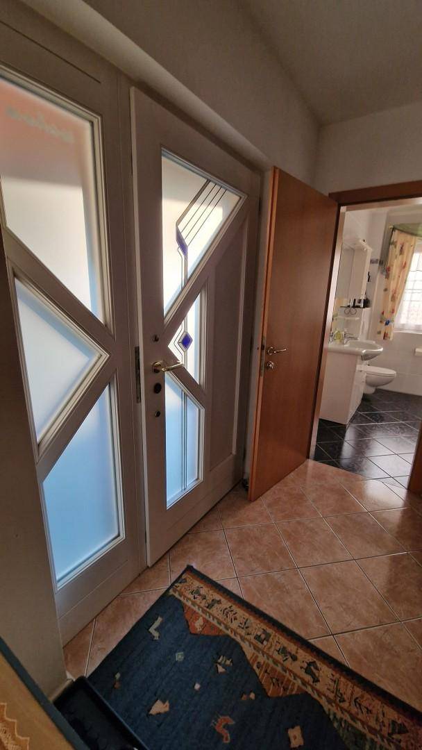 Eingangsbereich mit gefliestem Boden, modernen Glastüren und Blick ins Badezimmer.