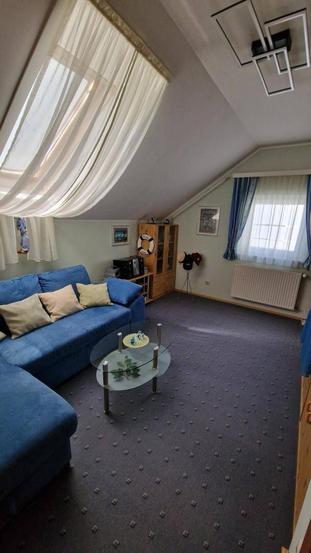Helles Wohnzimmer im Dachgeschoss mit blauem Sofa, Teppichboden und Dachfenster.