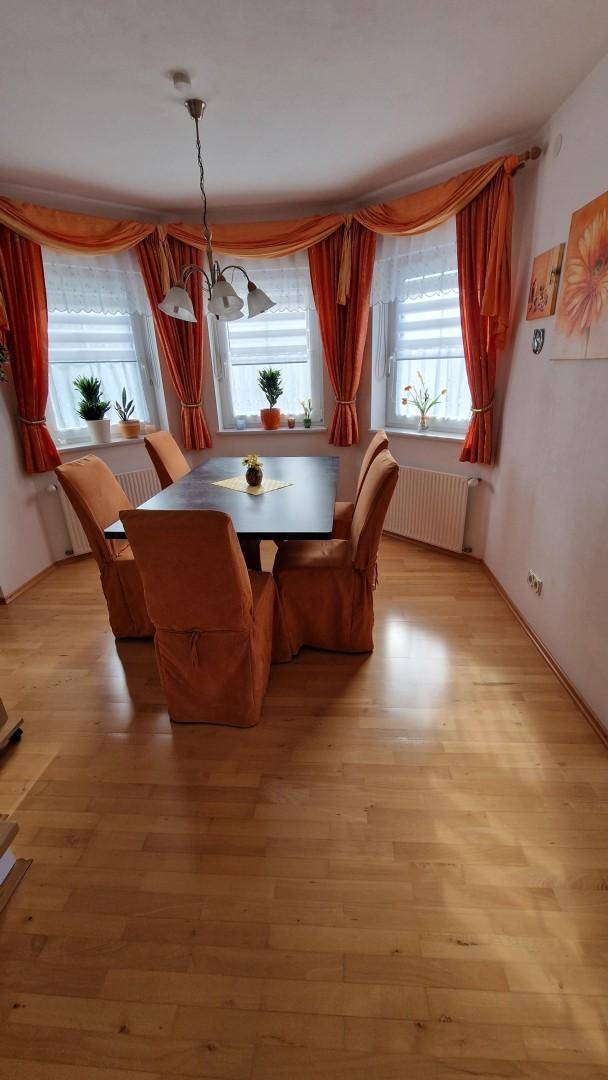 Heller Essbereich mit Holzfußboden, großem Esstisch und Fenstern mit orangefarbenen Vorhängen.