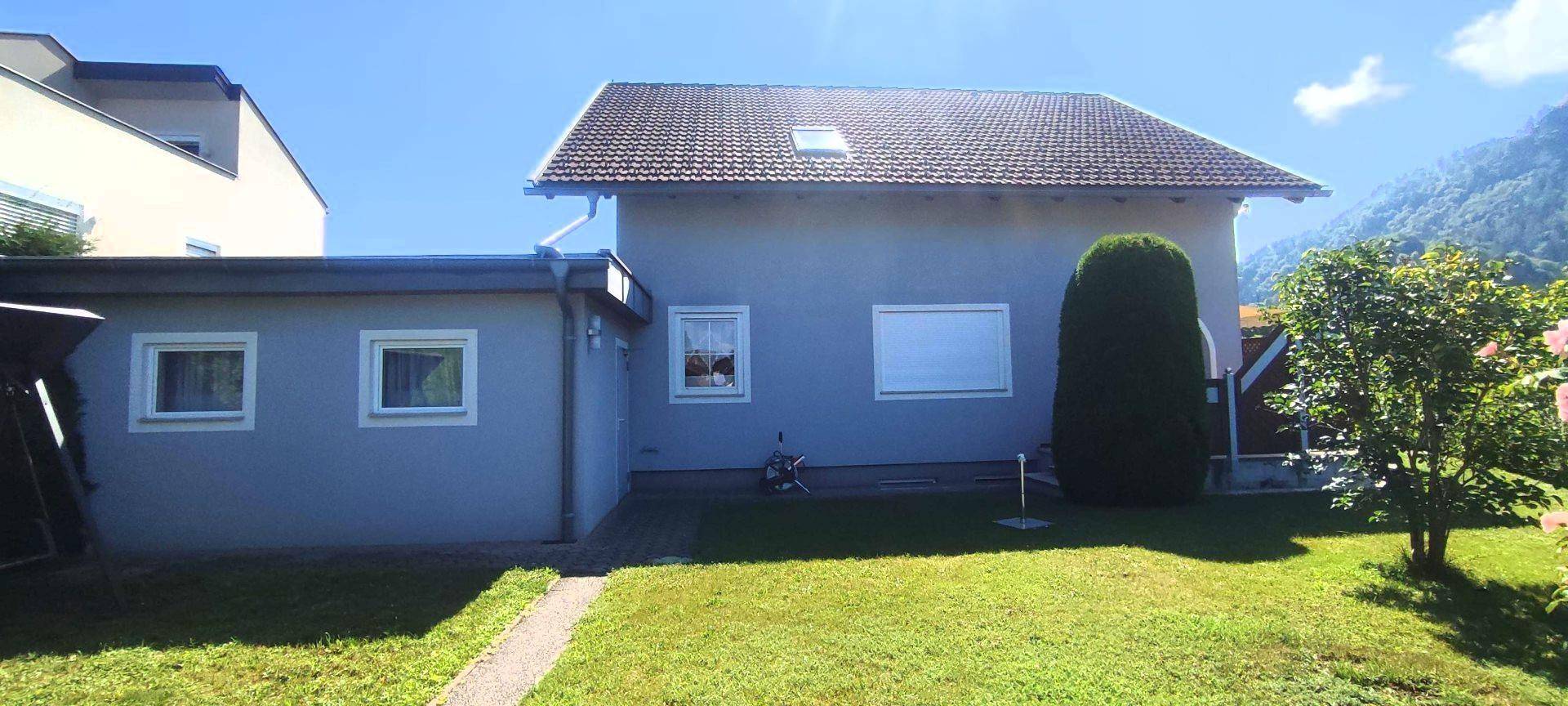 Rückseite des Hauses mit grünem Rasen, einem kleinen Baum und einem Dachfenster.