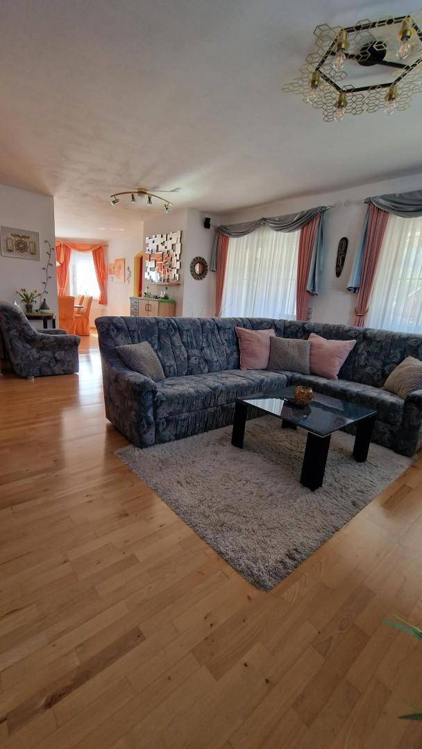 Geräumiges Wohnzimmer mit Holzfußboden, großem Ecksofa und einem flauschigen Teppich.