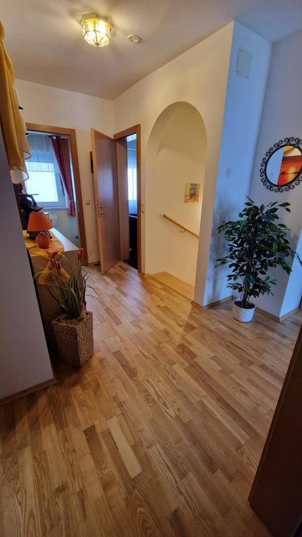 Heller Flur mit Holzfußboden, dekorativer Pflanze und einem Bogen zum Treppenbereich.