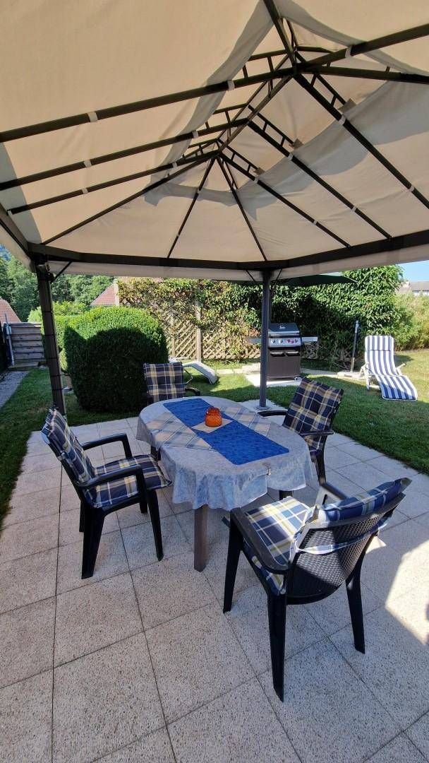 Gemütlicher überdachter Terrassenbereich mit Esstisch, Stühlen und Grill im Garten.