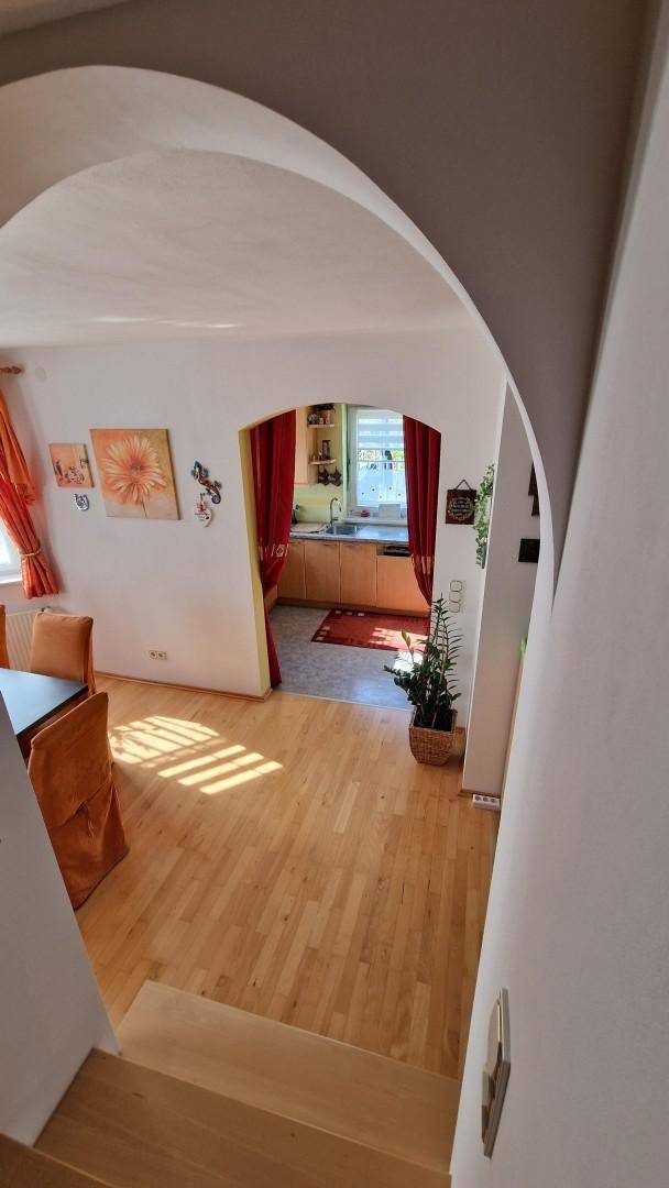 Essbereich mit Holzfußboden und Blick durch einen Bogen in die angrenzende Küche.