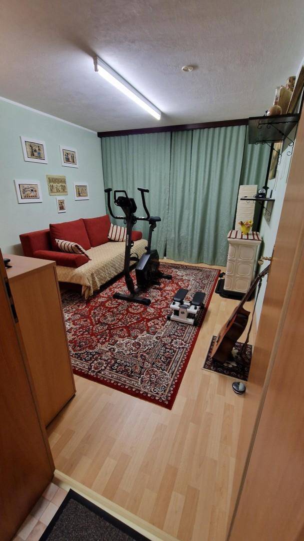 Fitnessraum mit Trainingsgeräten, Sofa, Teppichboden und grünen Vorhängen.