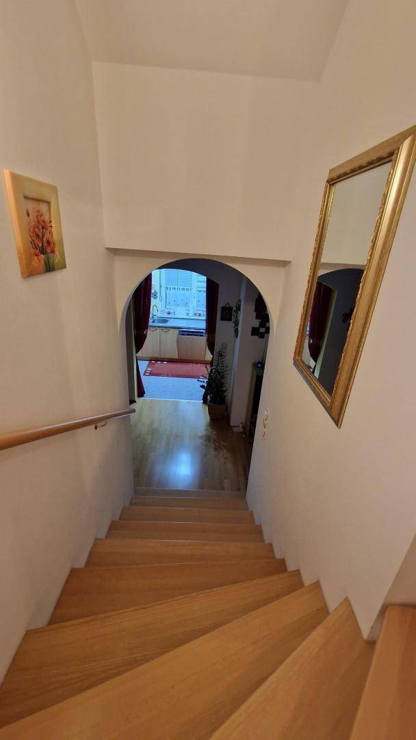 Holztreppe führt nach unten in einen hellen Flur mit Spiegel und dekorativen Elementen.