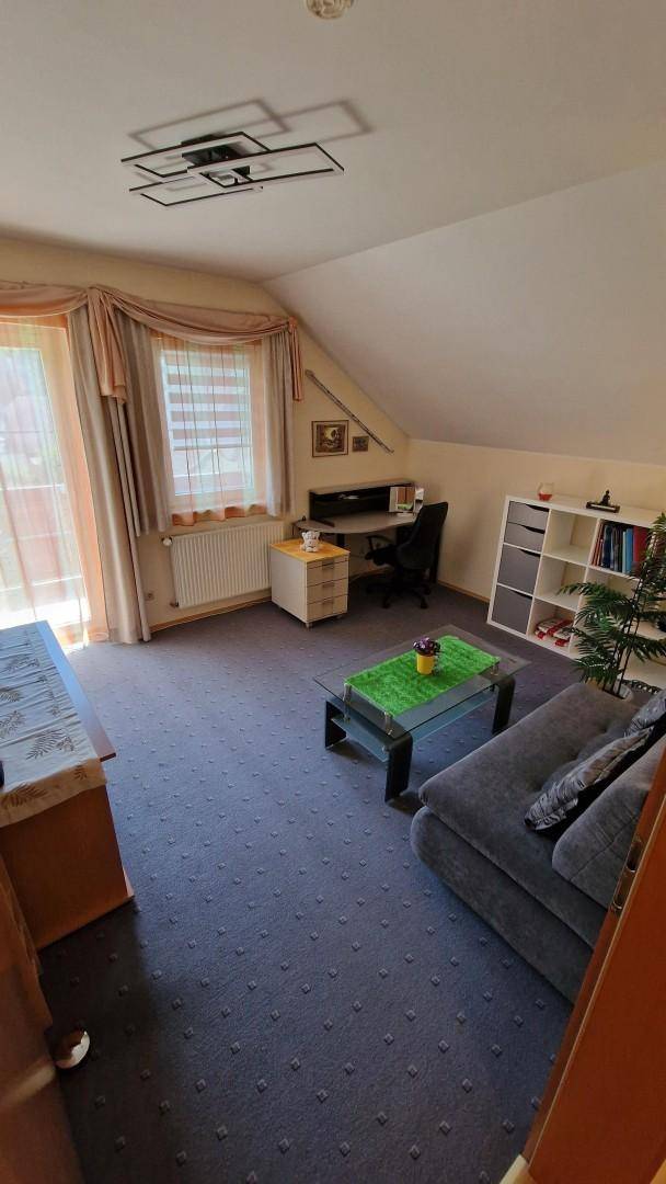 Arbeitszimmer im Dachgeschoss mit Schreibtisch, Sofa, Teppichboden und Dachschräge.