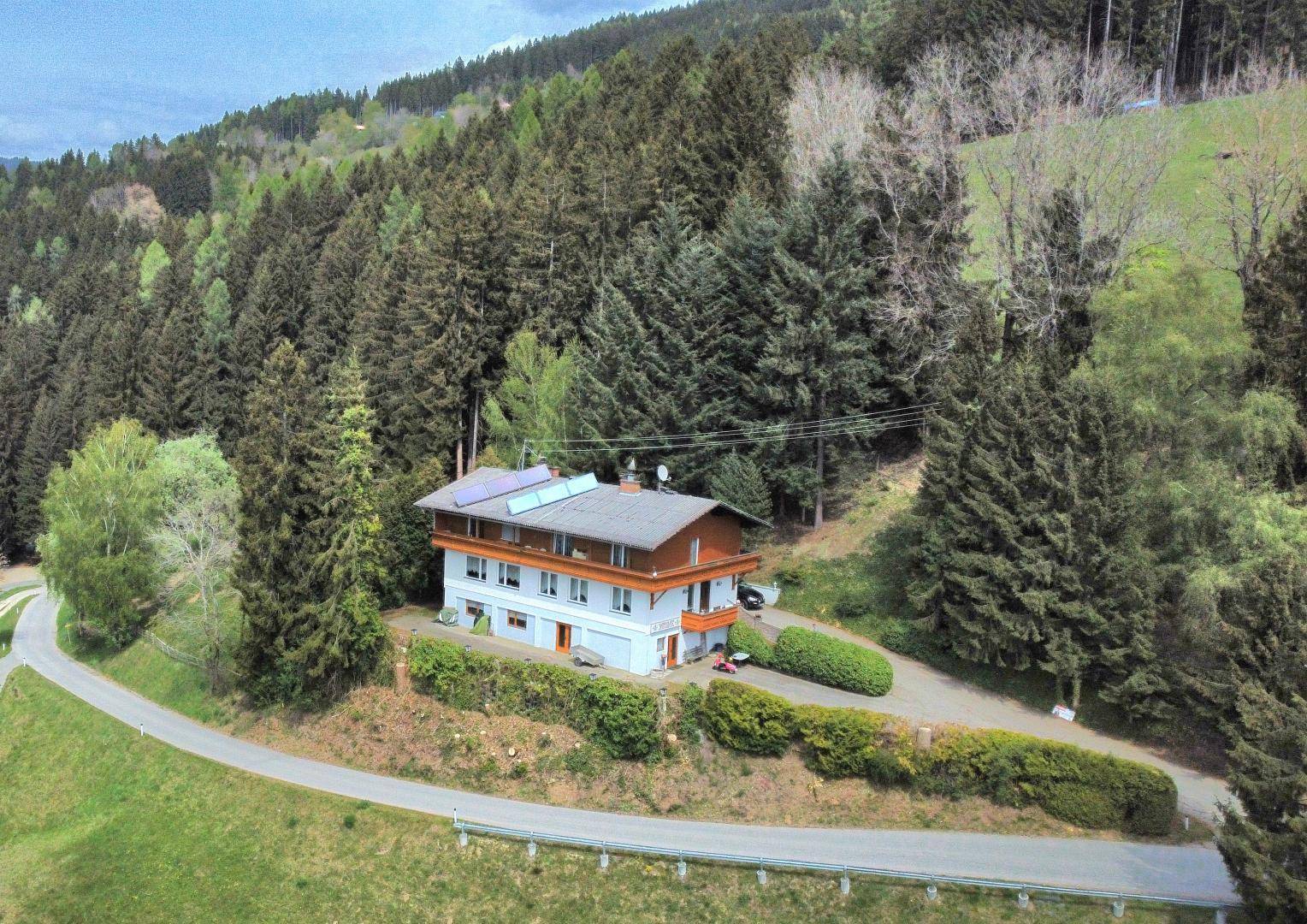 Luftaufnahme eines Hauses in ländlicher Umgebung, umgeben von Wald und mit Solaranlage auf dem Dach.