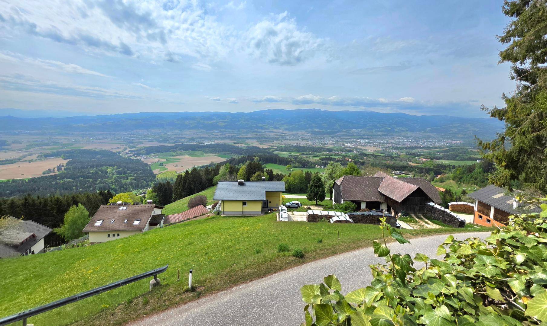 Weitläufige Landschaft mit grünen Wiesen, Wäldern und Häusern, die sich in die Hügellandschaft einfügen.