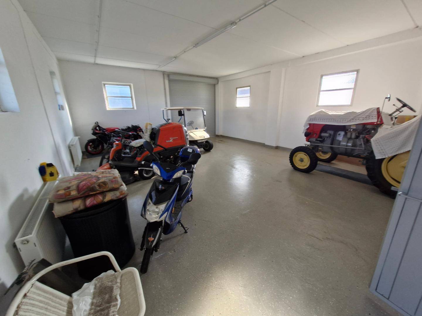 Geräumige Garage oder Lagerhalle mit verschiedenen Fahrzeugen und kleinen Fenstern.