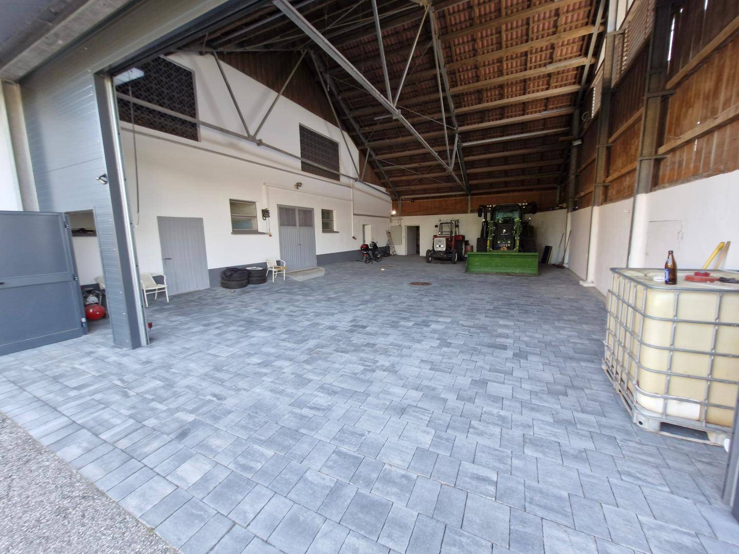 Große Halle mit gepflastertem Boden, hohen Decken und offenem Tor, ideal für landwirtschaftliche Nutzung.