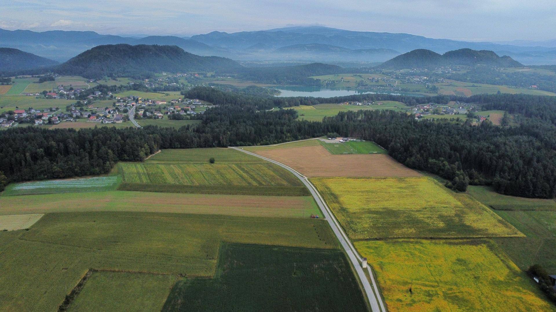 Weitläufige Luftaufnahme der ländlichen Umgebung mit Feldern, Wäldern und einem See in der Ferne.