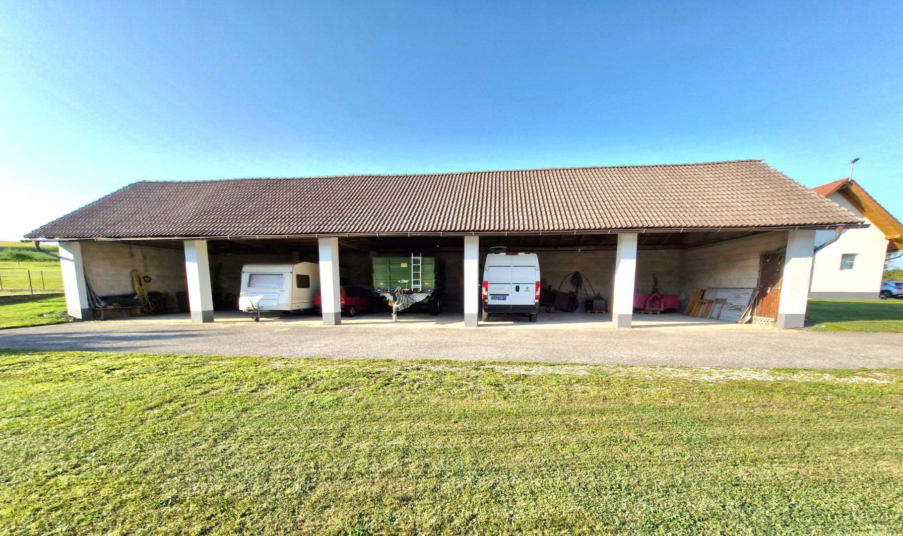 Offener Carport mit mehreren Stellplätzen für Fahrzeuge, umgeben von grünen Rasenflächen.