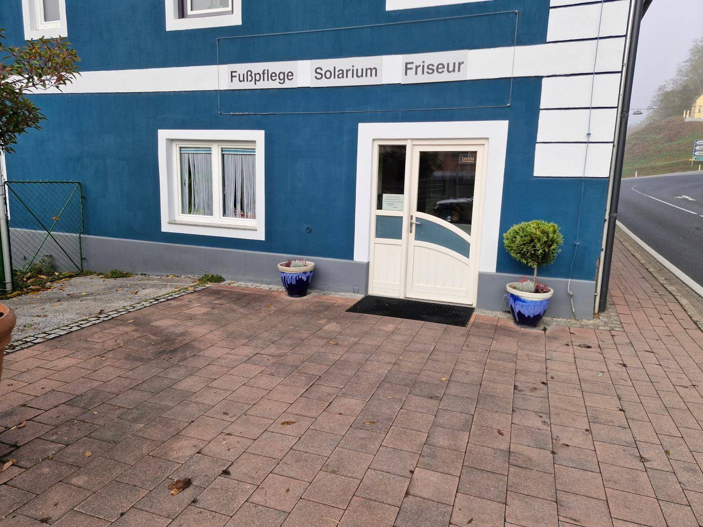 Eingangsbereich eines Geschäftsgebäudes mit blauer Fassade und Hinweisen auf Fußpflege, Solarium und Friseur.