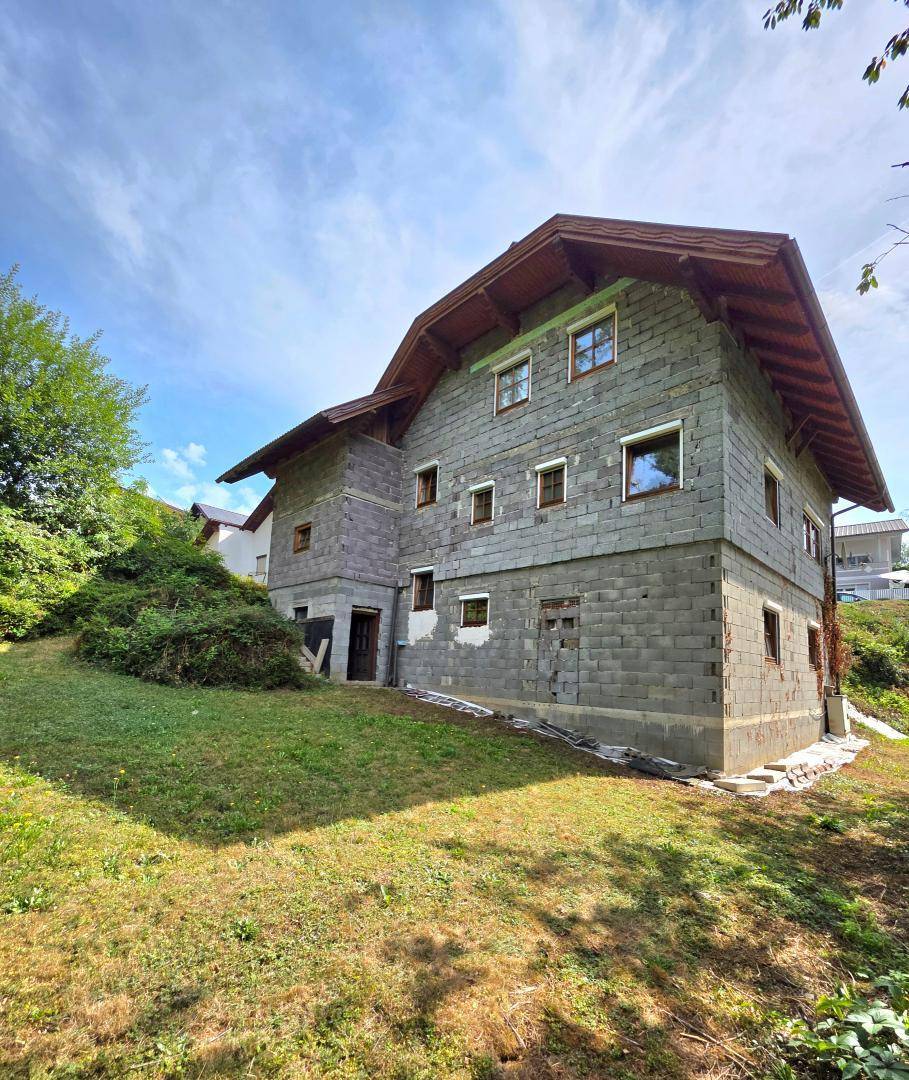Seitenansicht des Hauses mit Betonblockfassade, traditionellem Dach und umgebender Natur.