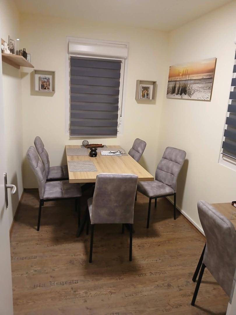 Esszimmer mit modernem Holztisch, grauen Stühlen und Fenster mit Jalousien.