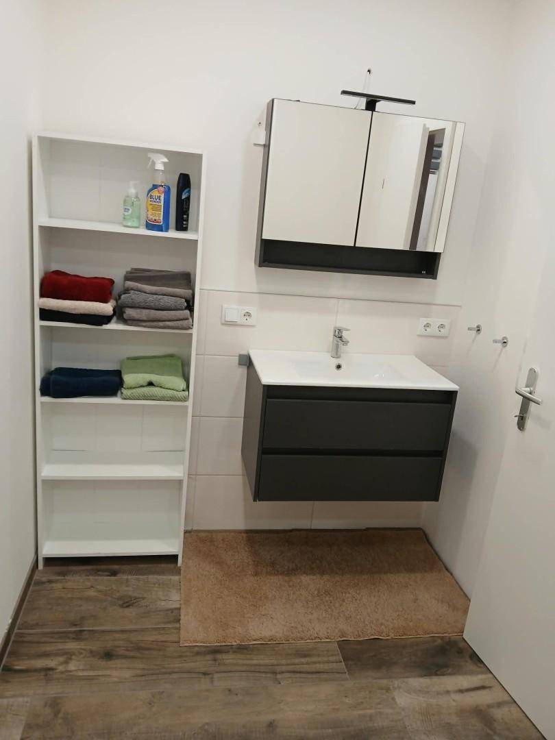 Badezimmer mit modernem Waschtischunterschrank, Spiegelschrank und offenem Regal.