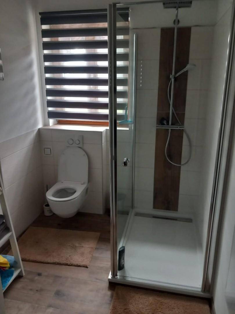 Modernes Badezimmer mit Duschkabine, wandhängendem WC und Fenster.