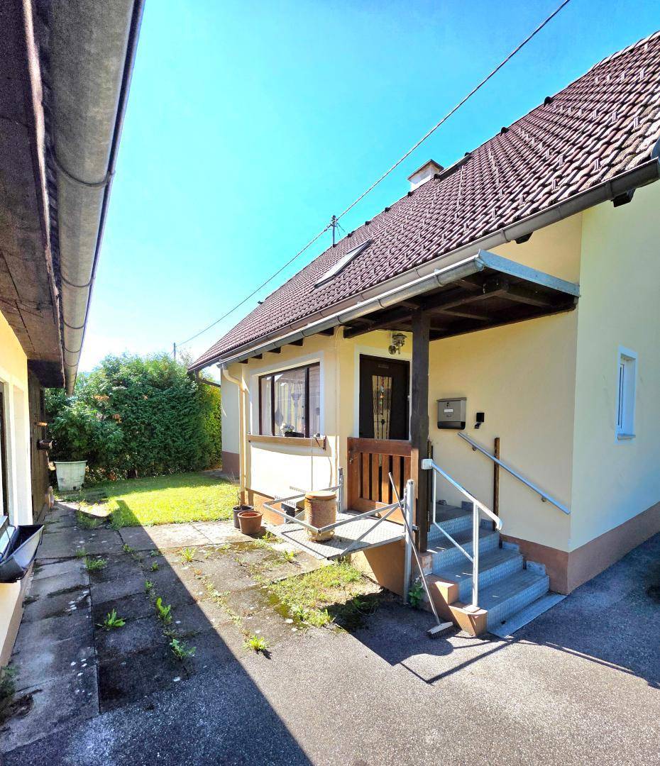 Eingangsbereich eines Hauses mit überdachtem Vorbau und Treppe, umgeben von einem kleinen Gartenweg.