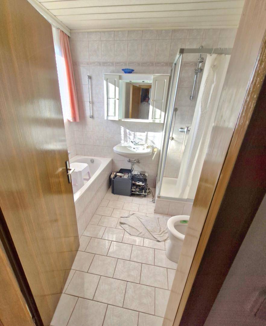 Badezimmer mit Badewanne, Duschkabine, Waschbecken und hellen Fliesen an Wänden und Boden.