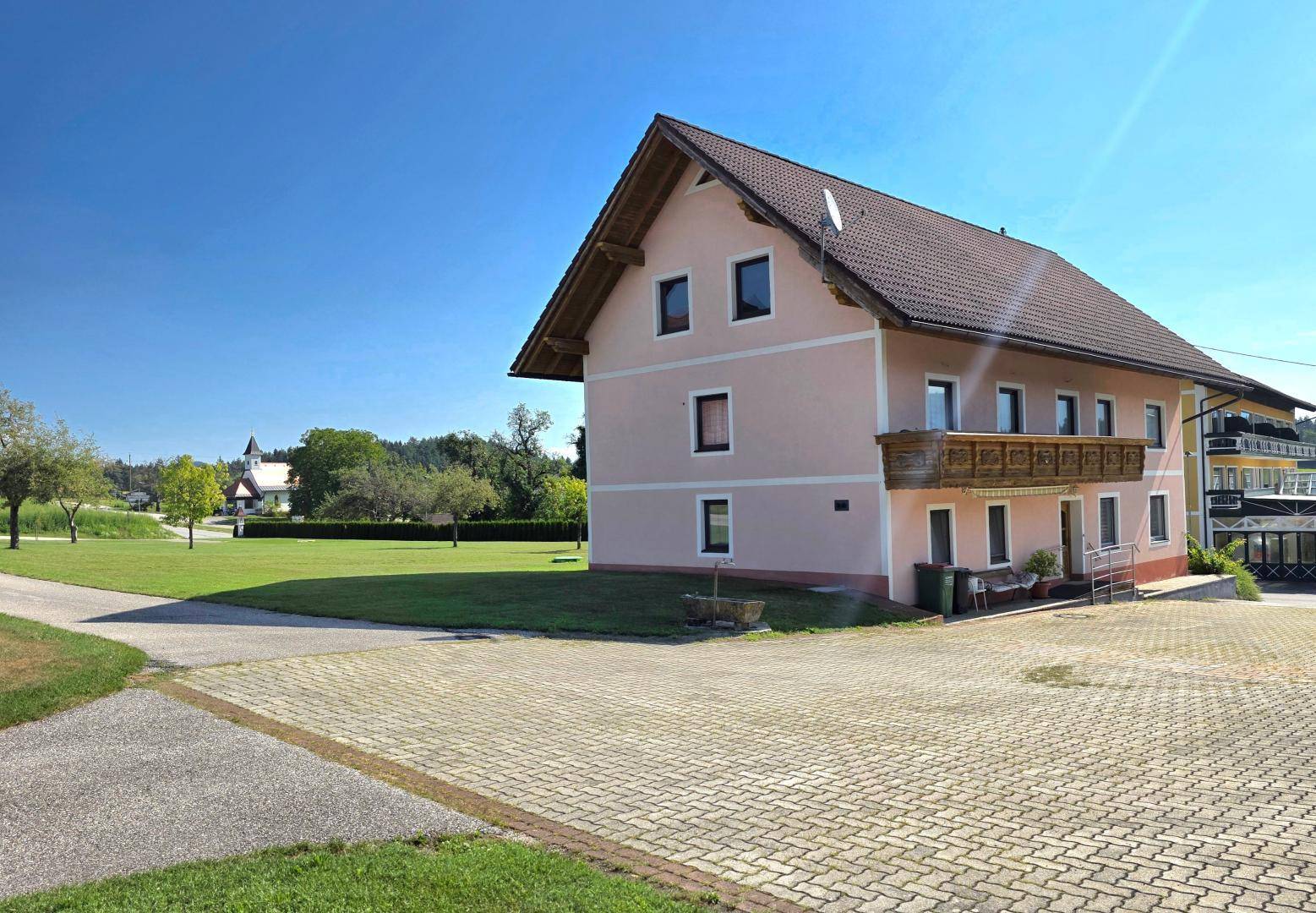 Ansicht des Hauses mit gepflasterter Zufahrt, Holzbalkon und Blick auf die ländliche Umgebung.