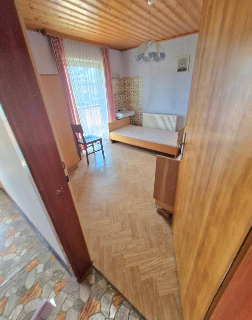 Schlafzimmer mit Einzelbett, Holzdecke, Laminatboden und Zugang zu einem kleinen Balkon.