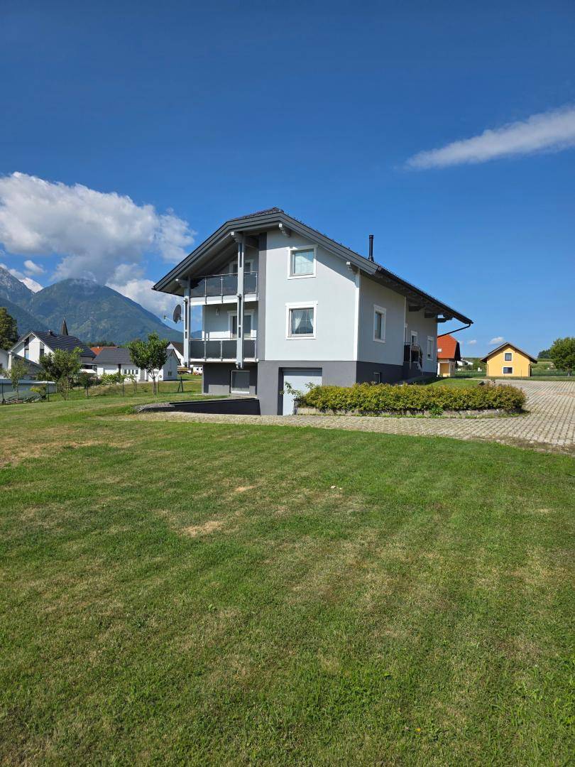 Modernes Einfamilienhaus mit Balkonen und Garage, gelegen in einer ländlichen Umgebung mit Bergblick.