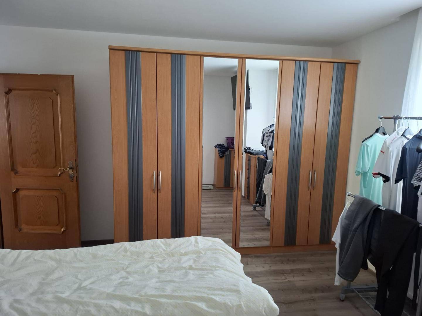 Schlafzimmer mit großem Spiegelschrank, hellem Laminatboden und einfacher Einrichtung.