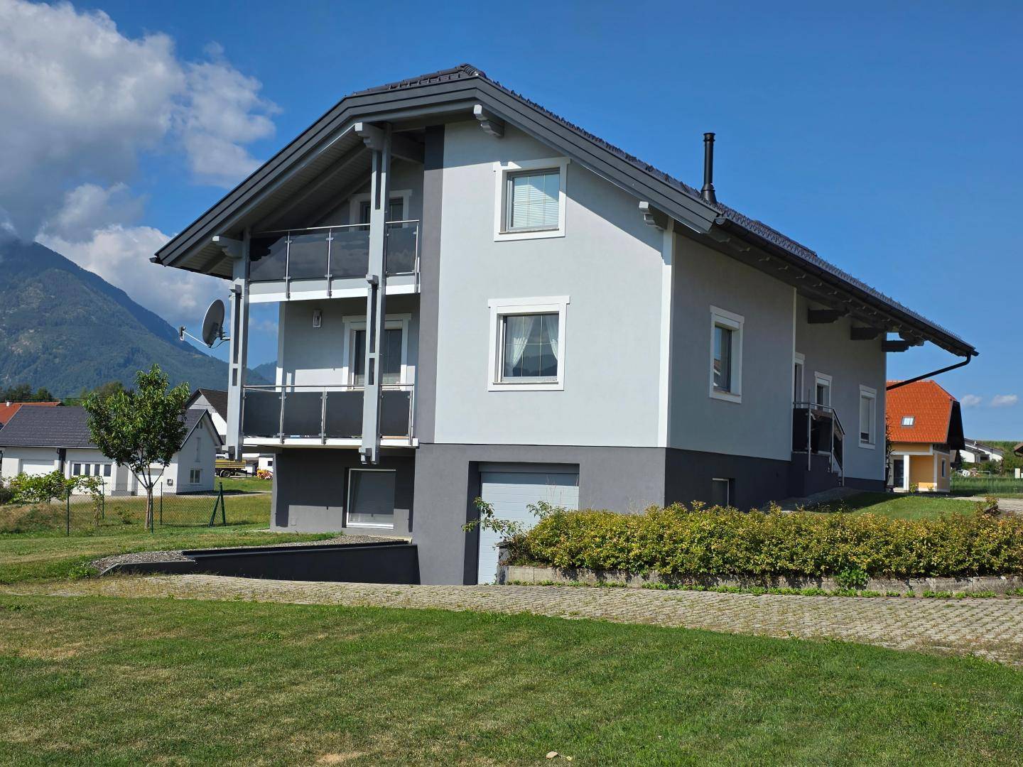 Modernes Einfamilienhaus mit Balkonen und Garage, gelegen in einer ländlichen Umgebung mit Bergblick.
