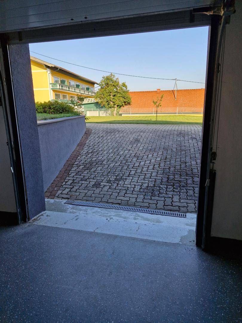 Blick aus der Garage auf die gepflasterte Einfahrt und das umliegende Grundstück.