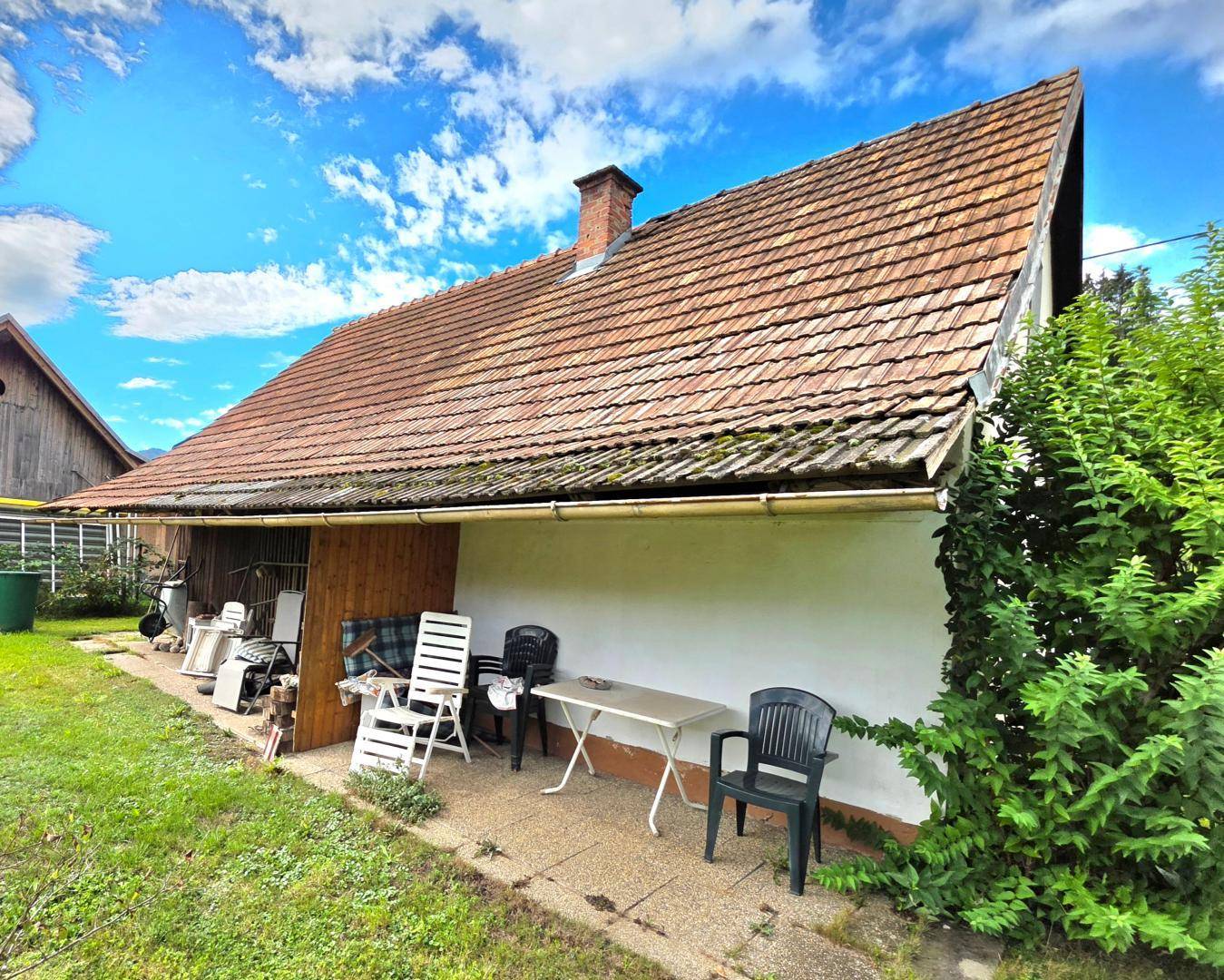 Kleine Terrasse am Haus mit Gartenmöbeln und Blick auf die grüne Umgebung unter blauem Himmel.