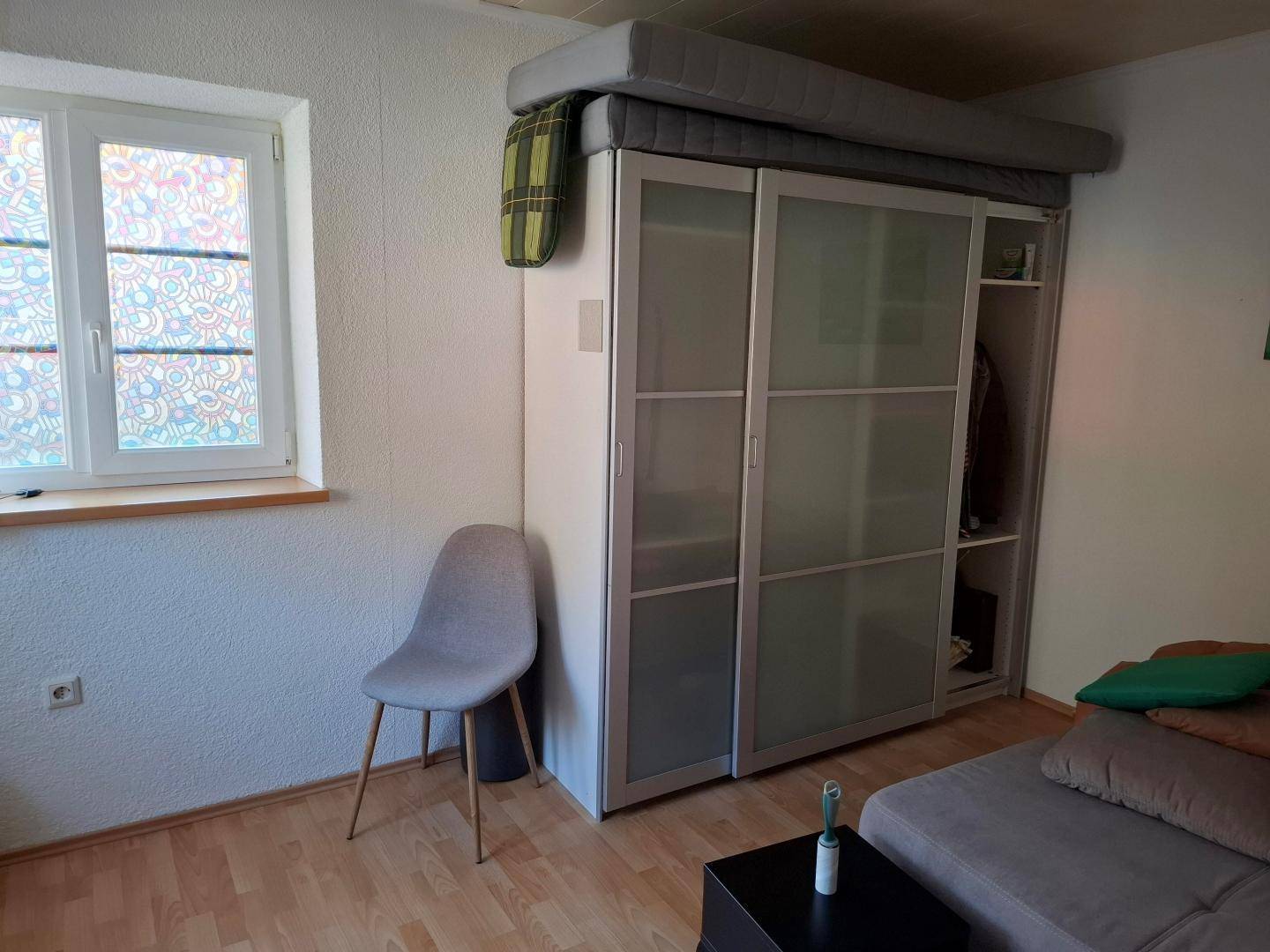 Schlafzimmer mit Schiebetürenschrank, Sofa und Fenster, bietet Stauraum und Gemütlichkeit.