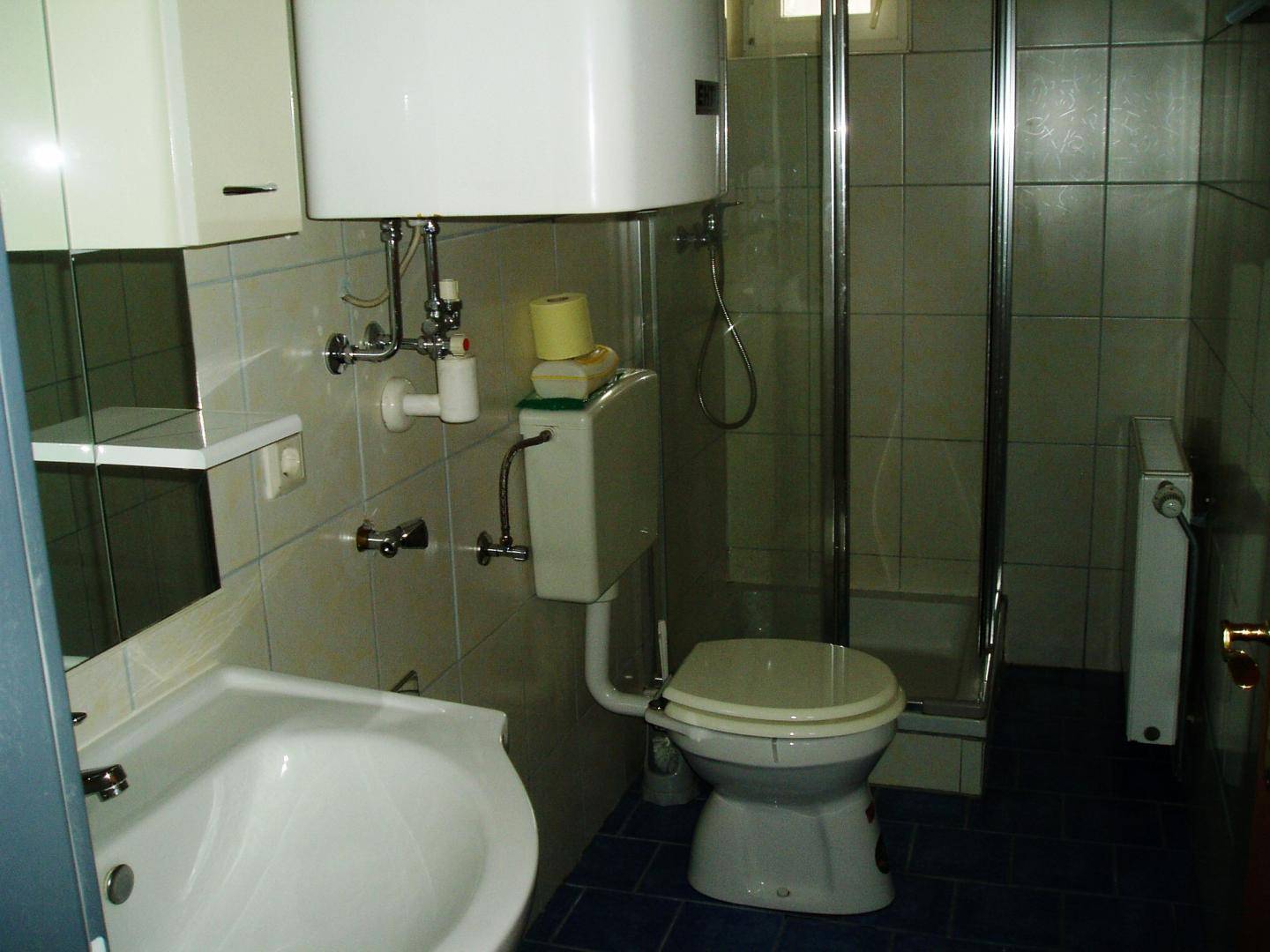 Badezimmer mit Dusche, WC, Waschbecken und blauen Bodenfliesen im Stil der 80er Jahre.