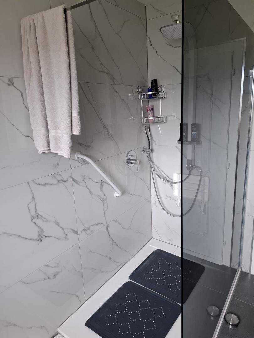 Modernes Badezimmer mit begehbarer Dusche, Marmorfliesen und Haltegriffen.