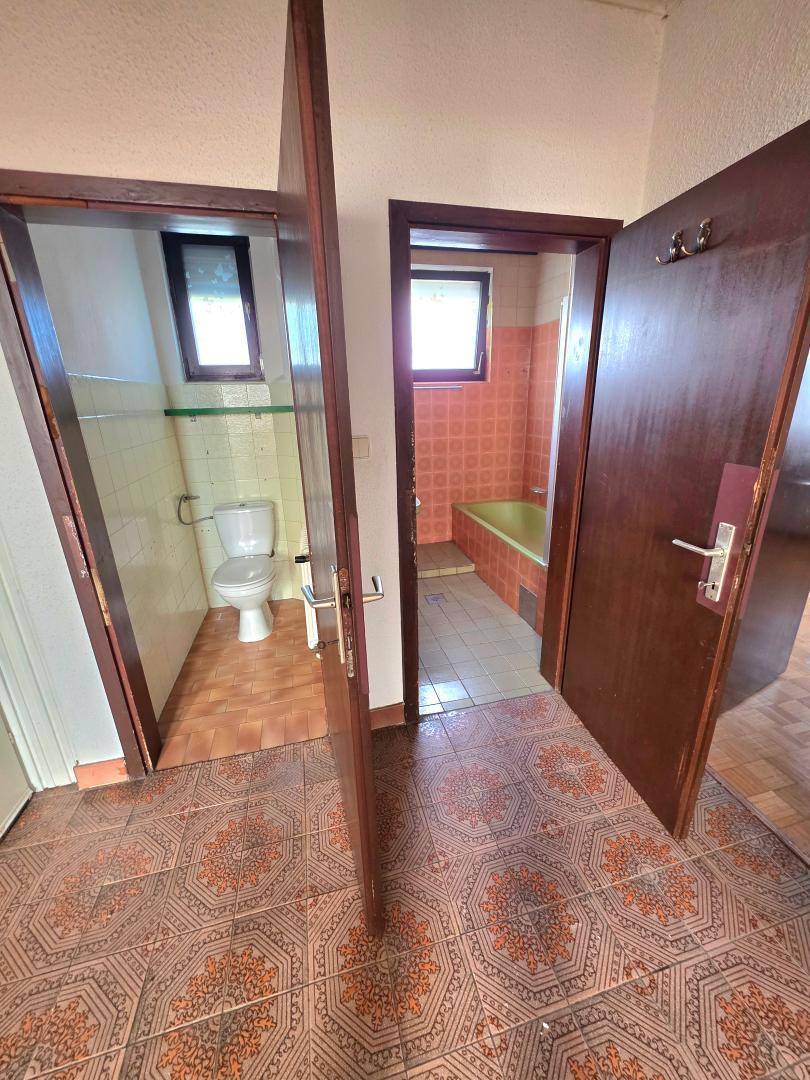 Flur mit Zugang zu einem WC und einem Badezimmer, beide mit älteren Fliesen und Armaturen.
