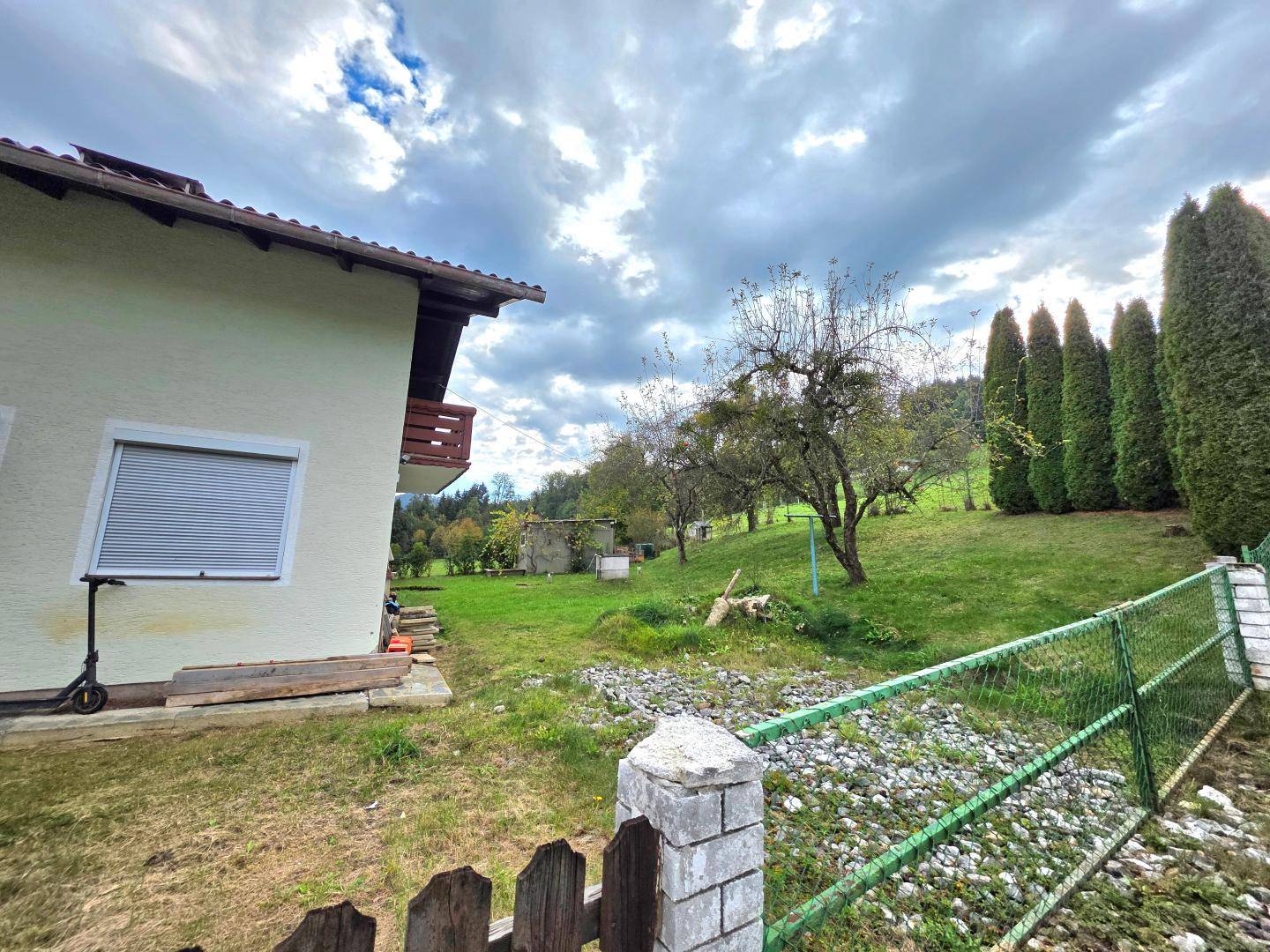 Gartenbereich neben dem Haus mit Zaun, Bäumen und Blick auf die umliegende Natur.