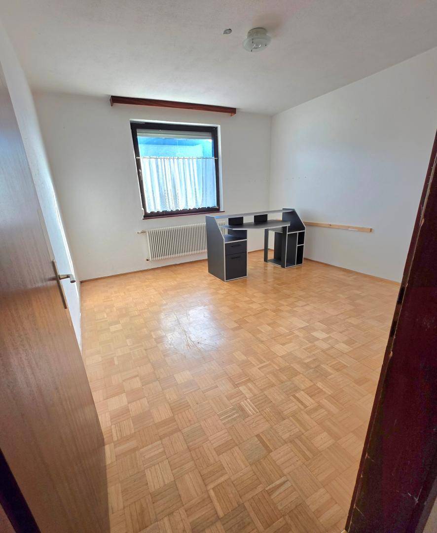 Schlafzimmer mit Parkettboden, Fenster und einem Schreibtisch, hell und funktional.