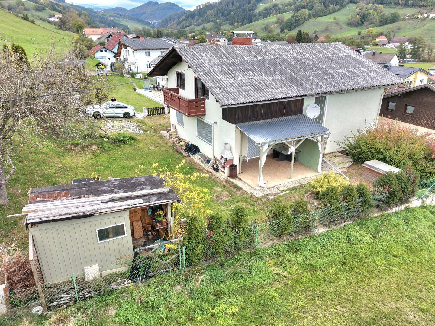 Gartenbereich hinter dem Haus mit Gartenhütte, Hecke und Blick auf die Hügellandschaft.