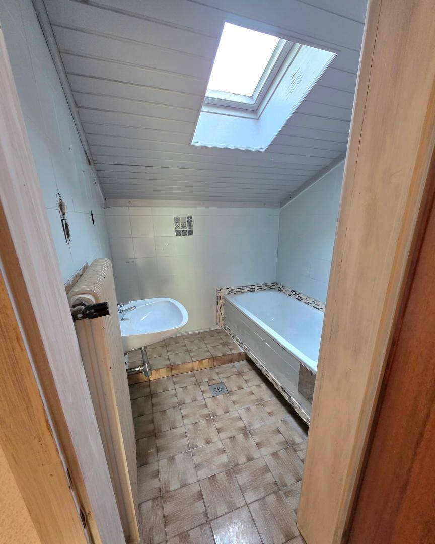 Badezimmer mit Badewanne, Waschbecken, Dachfenster und Holzverkleidung an der Decke.