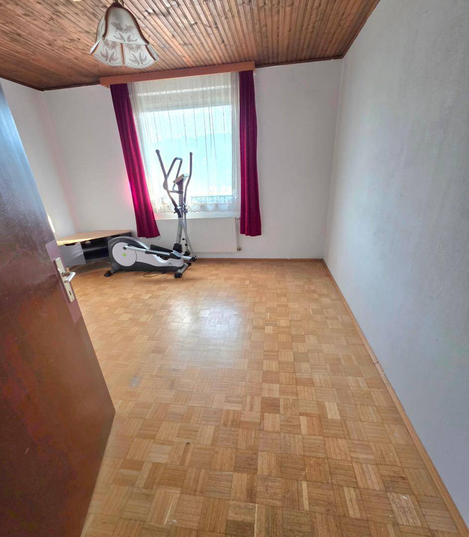 Zimmer mit Parkettboden, Fenster und einem Trainingsgerät, ideal für Sport oder Hobby.