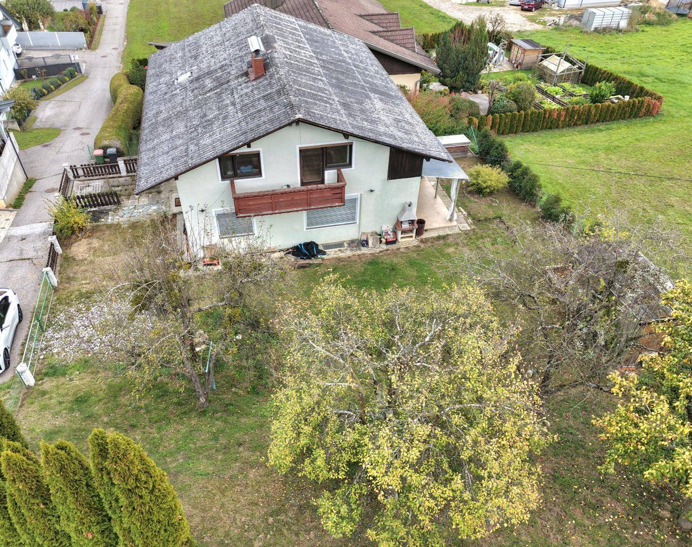 Luftaufnahme des Gartens mit Obstbäumen und dem Haus im Hintergrund, umgeben von Natur.