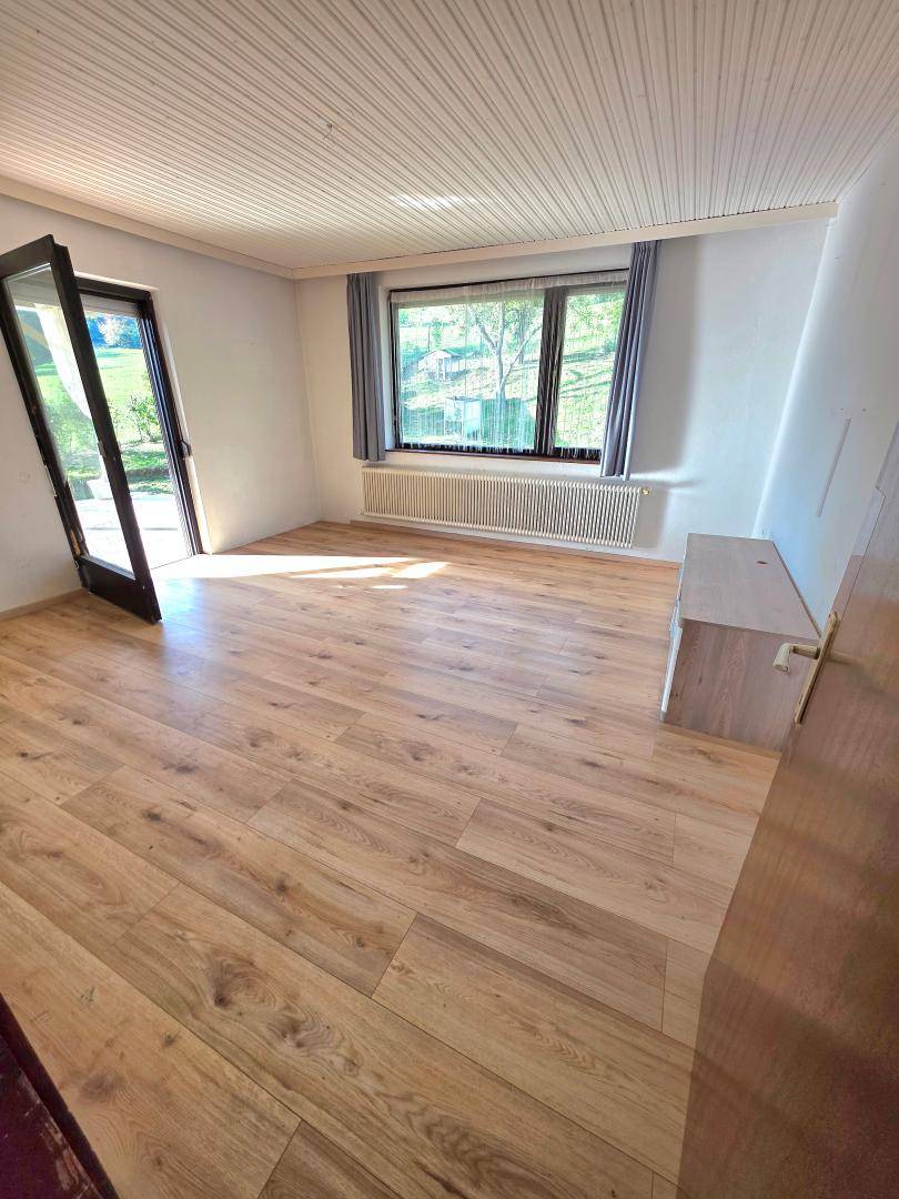 Heller Wohnraum mit Laminatboden, großem Fenster und Zugang zu einem Außenbereich.