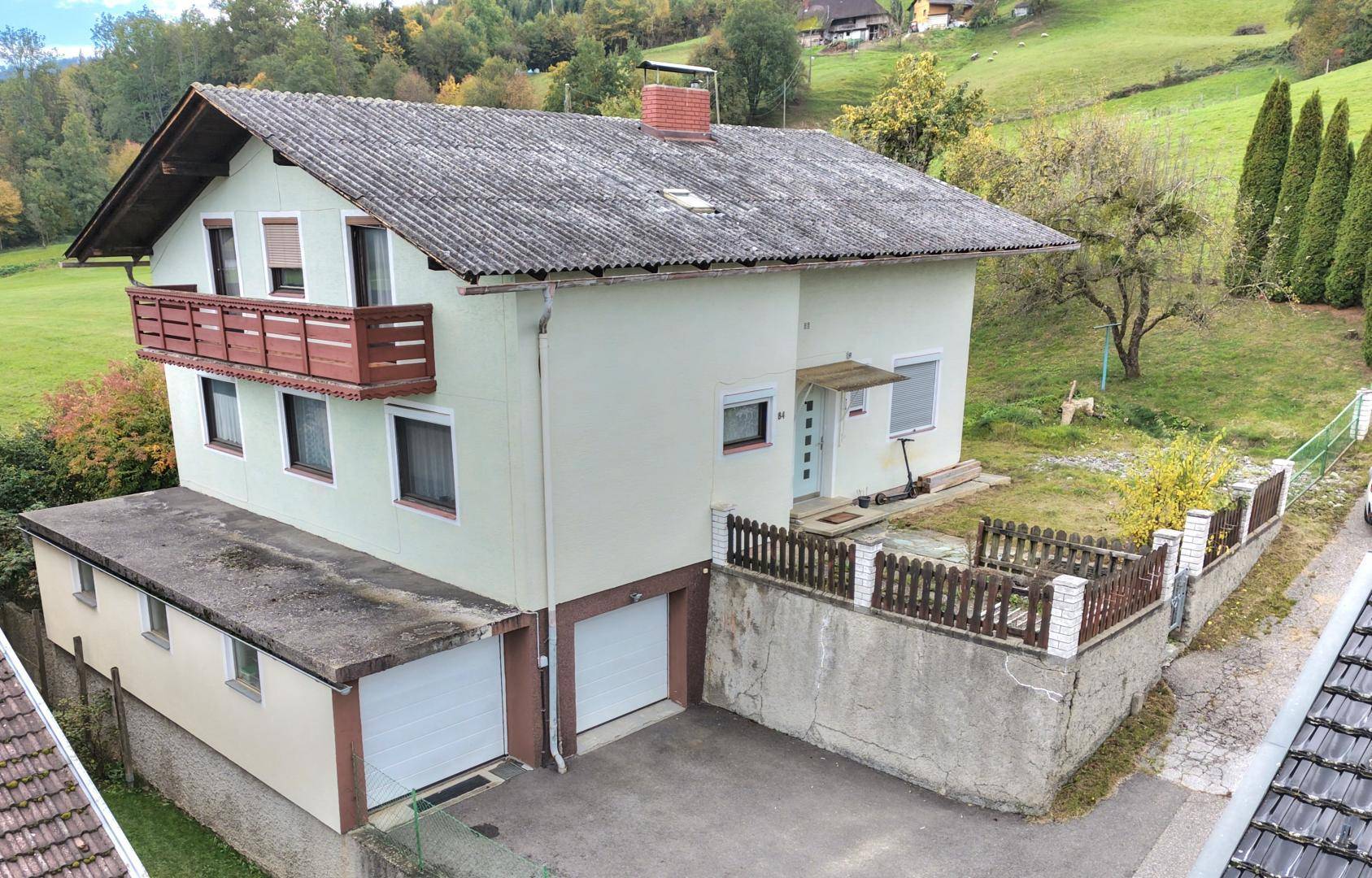 Einfamilienhaus mit Satteldach, Balkon und zwei Garagen in ländlicher Umgebung.