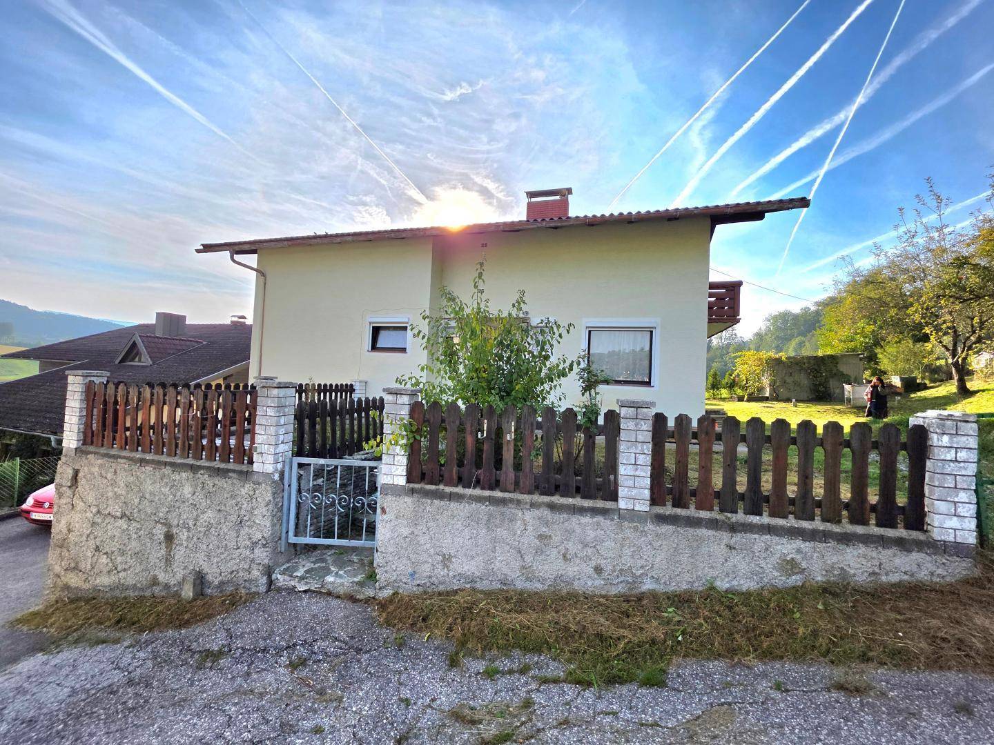 Vorderansicht des Hauses mit Zaun, Eingangsbereich und sonnigem Himmel.