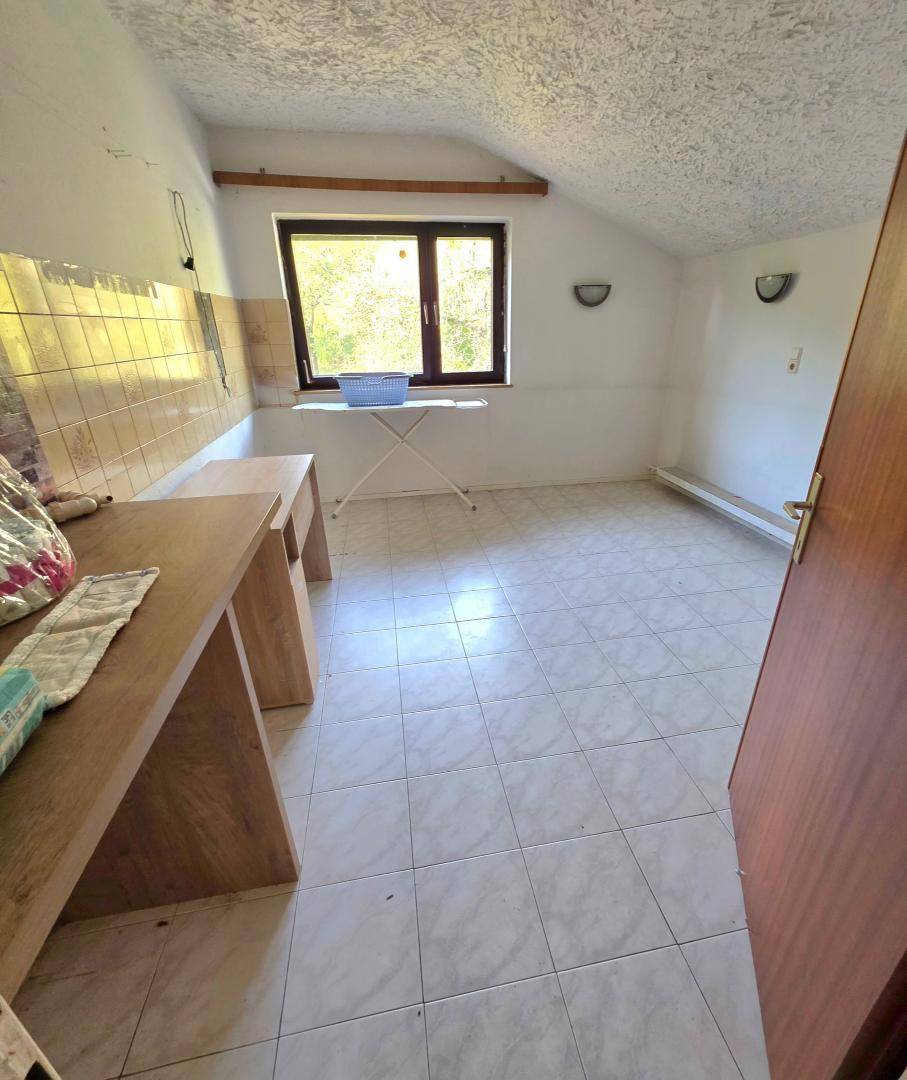 Funktionaler Raum mit Fliesenboden, Fenster und einfachen Holzstrukturen, ideal als Abstellraum.
