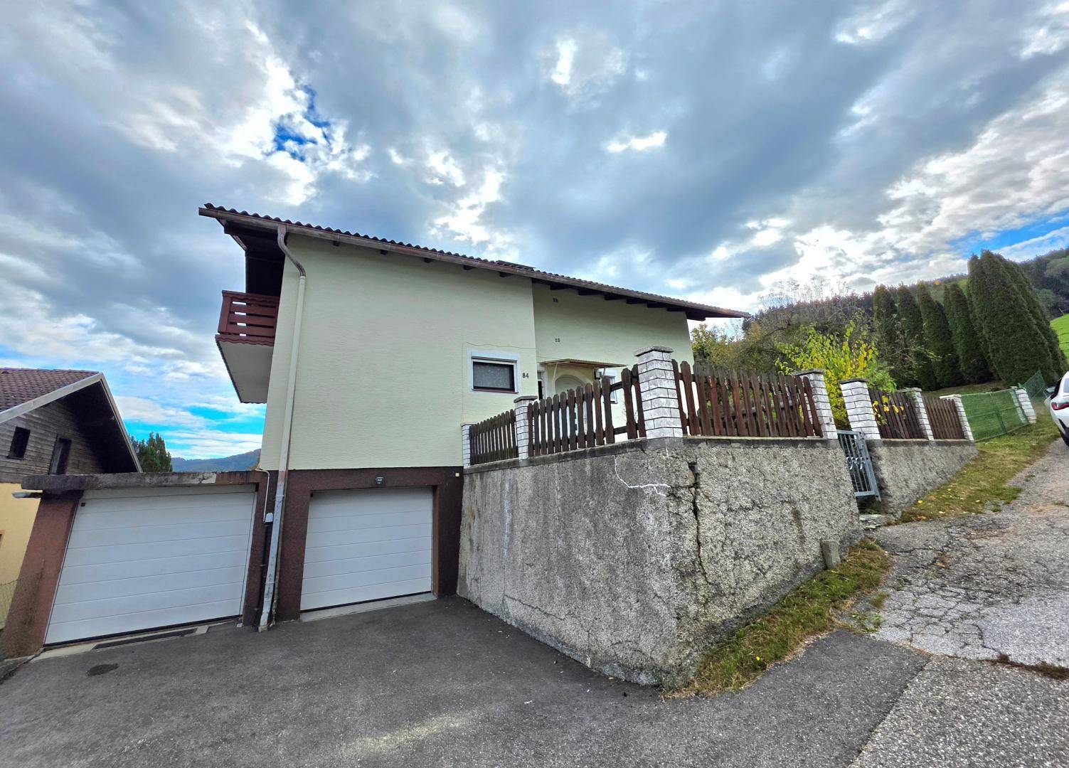 Seitenansicht des Hauses mit zwei Garagentoren und einer Stützmauer am Hang.