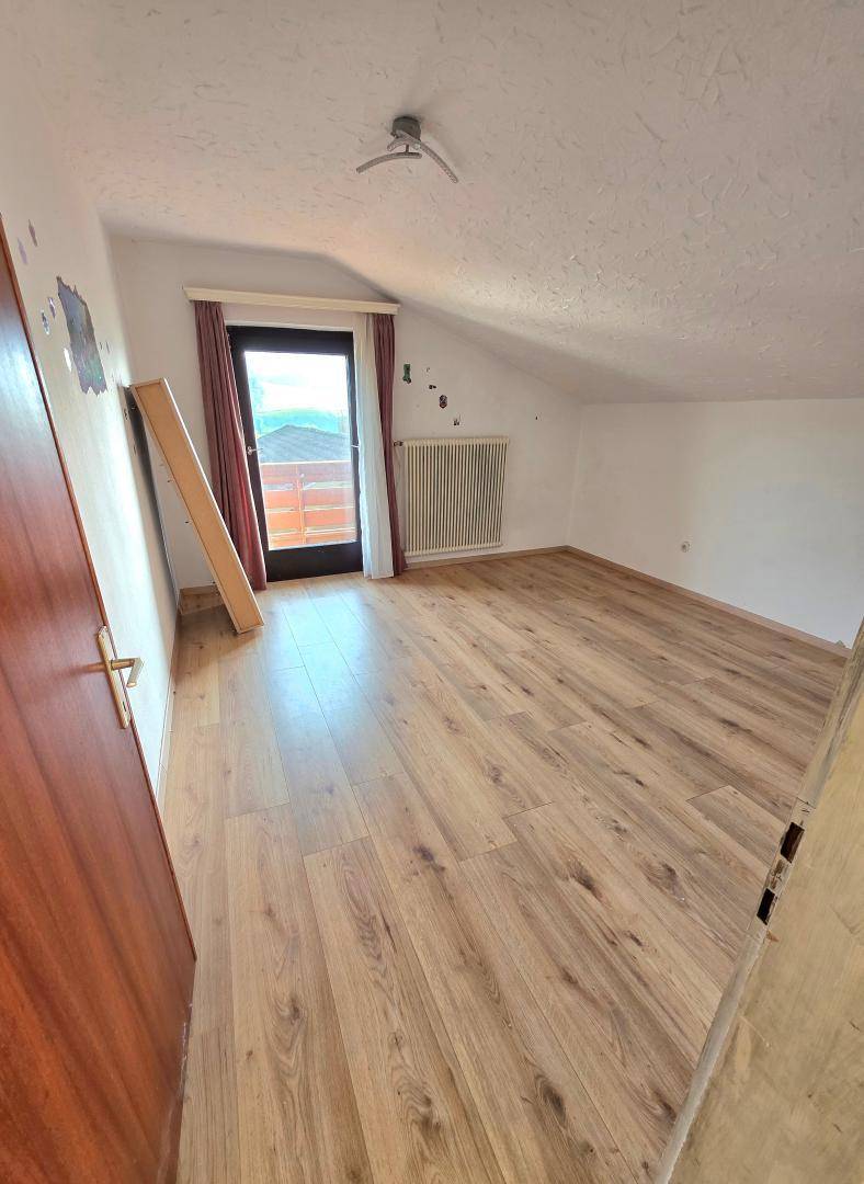 Schlafzimmer im Dachgeschoss mit Laminatboden, Zugang zum Balkon und Dachschräge.